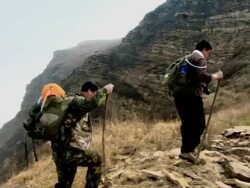 Chinese men hiking up a mountain ridge along stone rubble of the Great Wall of China.  Stock Footage