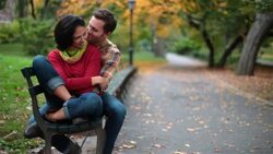 Boyfriend kisses girl on cheek in Central Park, couple nuzzles on park-bench (dolly-shot) Stock Footage