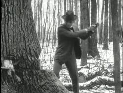 Henry Ford chops at a tree other the men use a saw to finish cutting it down. News Clip