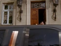 Tilt down long shot wealthy man and woman leaving hotel + getting into limousine / bellman loading luggage Stock Footage