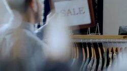Small business employee places SALE sign on shelf above clothing rack Stock Footage