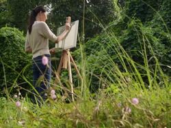 WS low angle view woman painting on an easel surrounded by nature. Stock Footage