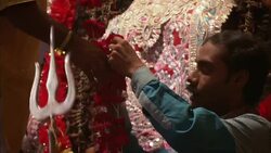 Two men drape a statue of the Hindu goddess Kali with strings of flowers. Stock Footage