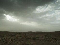 Dark clouds with small patches of light hang over the barren landscape.  Stock Footage