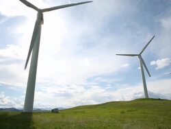 Wind turbines create electrical energy above meadow, mountains Stock Footage
