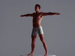 Wide shot young man in underwear standing on spinning turntable with arms outspread / London Stock Footage