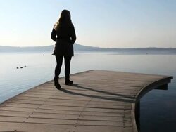 Boom upwards as woman walks along lake wharf, looks out Stock Footage