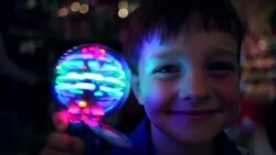 Young boy holds up spinning light to camera smiling in novelty shop looking surprised Stock Footage