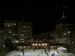 Busy outdoor ice skating rink in city surrounded by tall buildings at night - tilt down Stock Footage