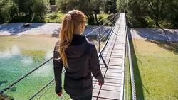 Young woman crossing a wooden suspension bridge over a stream Stock Footage