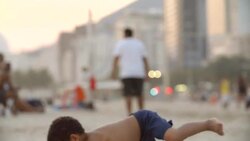 Cute Brazilian boy throws soccer ball in the air, falls and laughs in the sand on Copacabana Beach in slow motion Stock Footage