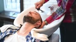 brutal hairdresser washes head of a bearded hipster Stock Footage