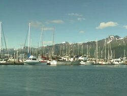 "View of boats in Seward Small Boat Harbor with rocky mountain top in Chugach National Forest, with partial snow, Seward, Kenai Peninsula, Alaska, blue skies." Stock Footage