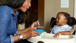 MS Smiling mother feeding infant son in highchair in dining room Stock Footage