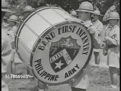 1939: COMMONWEALTH of the PHILIPPINES: DEFENSE: First Infantry Division Philippines Army Band (TABAK) w/ Filipino men in uniforms playing tubas, CU drum. WS Color Guard standing holding US, Philippines & Coat of Arms flags w/ soldiers marching BG. Instructional Video