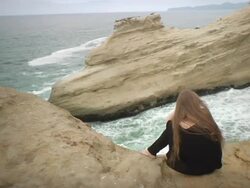 WS ZI Girl sitting on cliff with sea in background / Cape Kiwanda, Oregon, USA Stock Footage