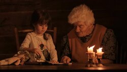 A young girl and grandmother read a book by the light of candles Stock Footage