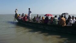 A wooden boat crammed with passengers prepares to leave the riverbank and cross a wide expanse of open river in Northern Bangladesh Stock Footage