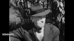 1950: SENIOR SEDENTARY LIFESTYLE: Elder male in suit & hat sitting on park bench, others walking by. Three Senior males sitting on public bench, one man reading.  Inactivity, Depression, Unhealthy Lifestyle, relaxing, resting. Instructional Video