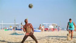 Brazilian player shoulders ball to partner who sets him up for dynamic header in beach footvolley match Stock Footage