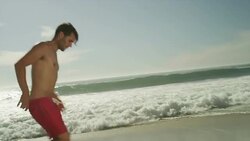 Young man kicking soccer ball on beach Stock Footage