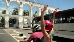 Girl throws hands in the air and cheers as mototaxi drives under the Lapa Arches Stock Footage
