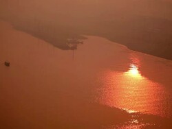 Pink evening sun shimmers down on reflective wide expanse of river with far bank and lone rowing boat in view.  India Stock Footage