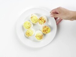 CU Woman hand entering setting down round white plate with six slices deviled eggs with paprika / Omaha, Nebraska, United States Stock Footage