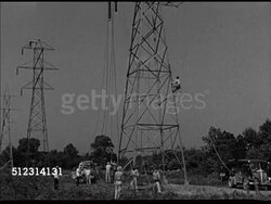 1947: POWER LINE CONSTRUCTION: VS Technicians setting up power lines for towers, on ladder scaffolding high above at top of tower, workers below operating wire spool, technician signaling from top of tower. Electric power transmission, electricity Instructional Video