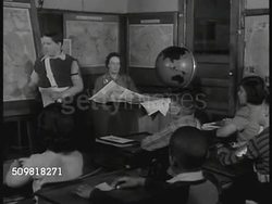 1944: SCHOOL: EXT Buckingham School. INT Classroom w/ boy at map, problem pronouncing a city in Poland (Lwow), young girl of Polish decent helping him. INT Classroom w/ girl at map of Brazil, talking about races there, children & teacher listening. Instructional Video