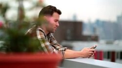 Hip young man on Brooklyn rooftop quickly scans smartphone (dolly-shot) Stock Footage