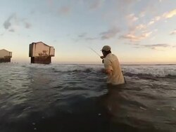 WS Man casting fly rod in surf with abandoned building in distance at sunset / Iztapa, Guatemala Stock Footage