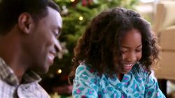 Father looks on as his girl tears open her Christmas present and admires her new pink sweater Stock Footage