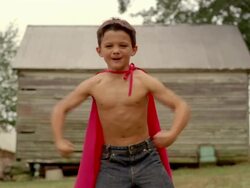 Medium shot selective focus shirtless boy wearing a red cape / flexing muscles and making faces Stock Footage