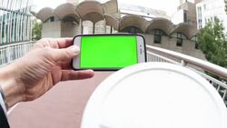 Man holding a smartphone with a green screen, while raising a coffee cup to his mouth Stock Footage