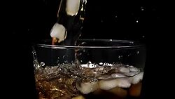 Pouring cola soda into glass of ice with splashes at slow motion on black background Stock Footage