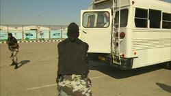 Arab dissidents exit a white bus with their hands above their heads as soldiers point guns at them. Stock Footage