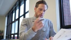 Architect with blueprints entering and sitting in office Stock Footage