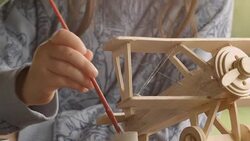HD Sequence. GENDER NEUTRAL KIDS. Happy Child Painting a Wooden Airplane Model on a Beautiful Summer Morning at The Porch. Stock Footage