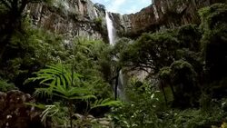 Man traverses highline stretched above waterfall, valley Stock Footage