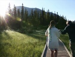Couple walk along mountain boardwalk towards sunrise Stock Footage