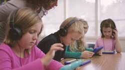 Elementary school aged children working on digital media tablets with teacher in classroom Stock Footage