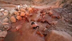 Young hiker boy sits down in river to cool off during a hike in a Utah canyon narrow Stock Footage