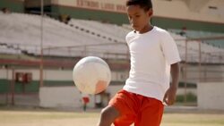 Brazilian boy kicks up dirt as he juggles soccer ball on dry stadium field Stock Footage