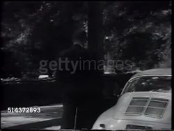 1966: STARK DILLARD: CU Stark smoking cigarette while driving car in town, WS Porsche 911 moving downtown road. Reverend Stark getting out of parked Porsche, walking toward St. Paul's Episcopal church, through breezeway, into building. Instructional Video