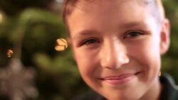 Cute young boy looks up and smiles at camera in front of Christmas tree Stock Footage