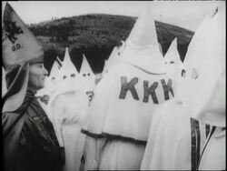 The Ku Klux Klan stands around burning cross at night. News Clip