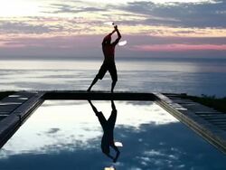 WS Male poi dancer without shirt performing with fireballs in front of pool with reflection of his silhouette in pool at sunrise / Montezuma, Costa Rica Stock Footage