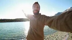 Cheerful man in nature takes selfie portrait near lake Stock Footage