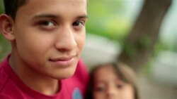 Hispanic teenage brother stares into camera, younger sister gazes at him admiringly Stock Footage